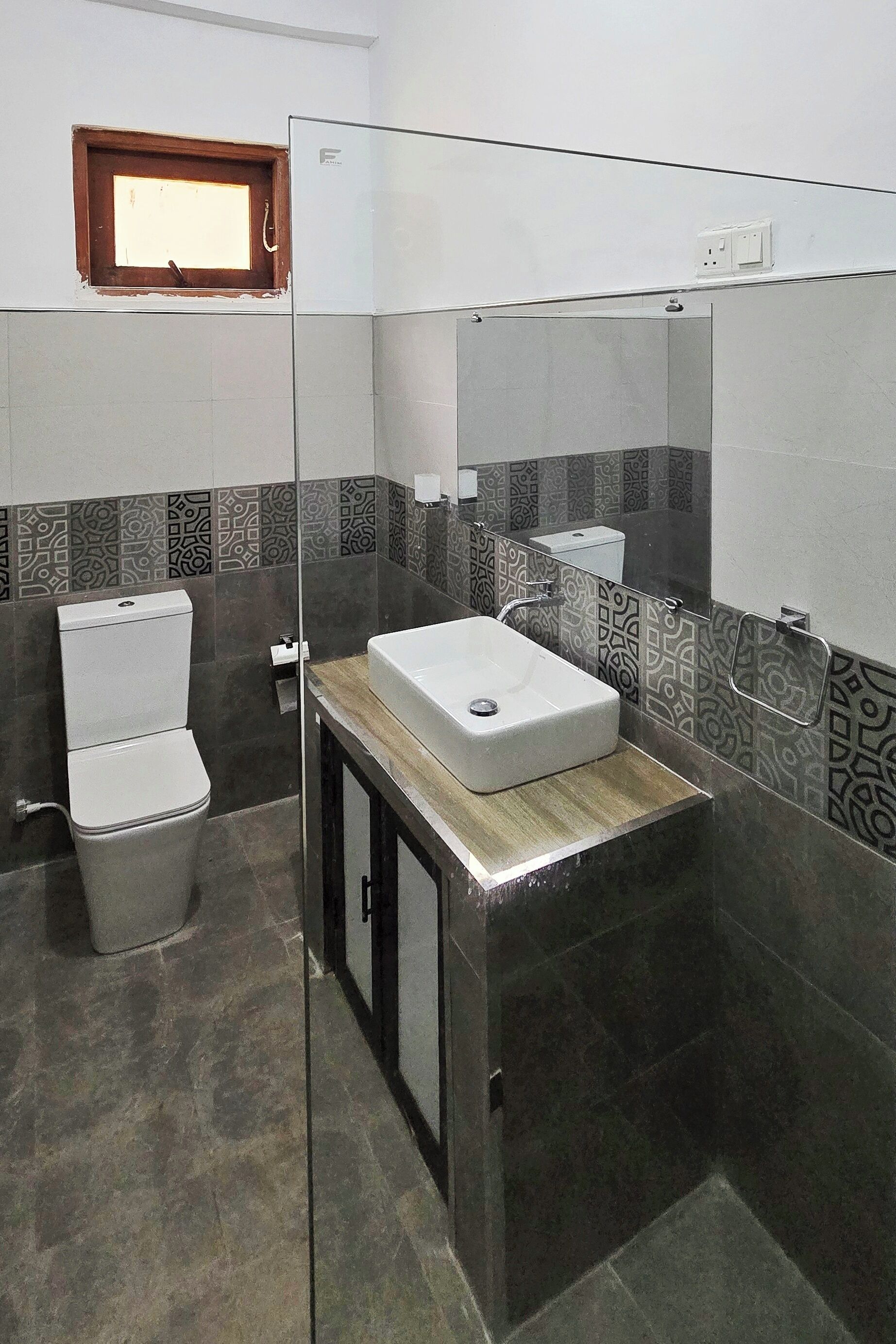 A bathroom with a toilet, a sink, a mirror, and patterned tiles.