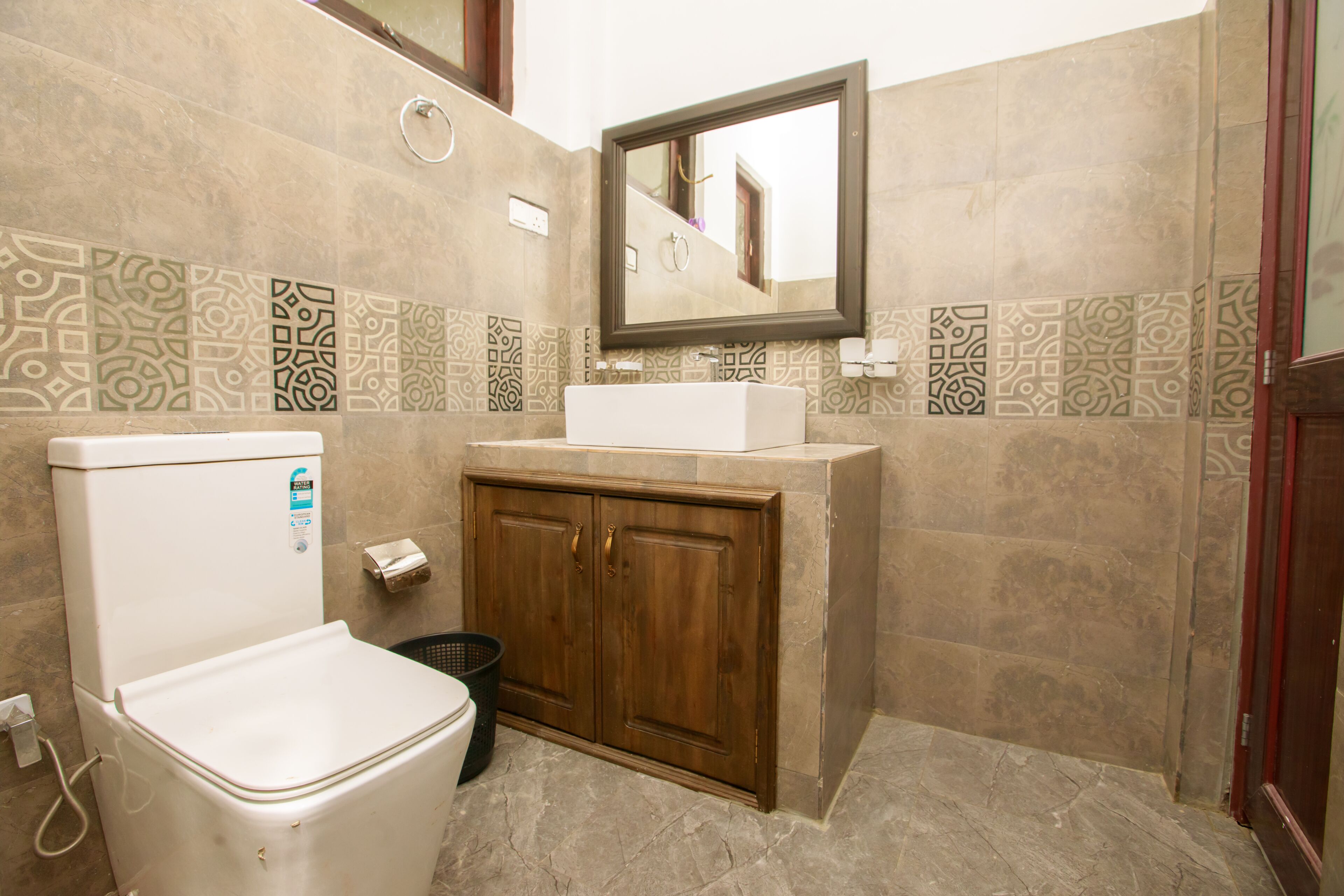 A bathroom with a toilet, sink, cabinet, and patterned tiles.