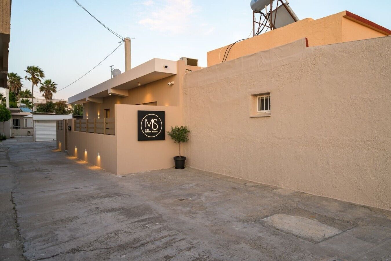 A modern building with a minimalist design, featuring a logo on the facade, a small window, and a potted plant.