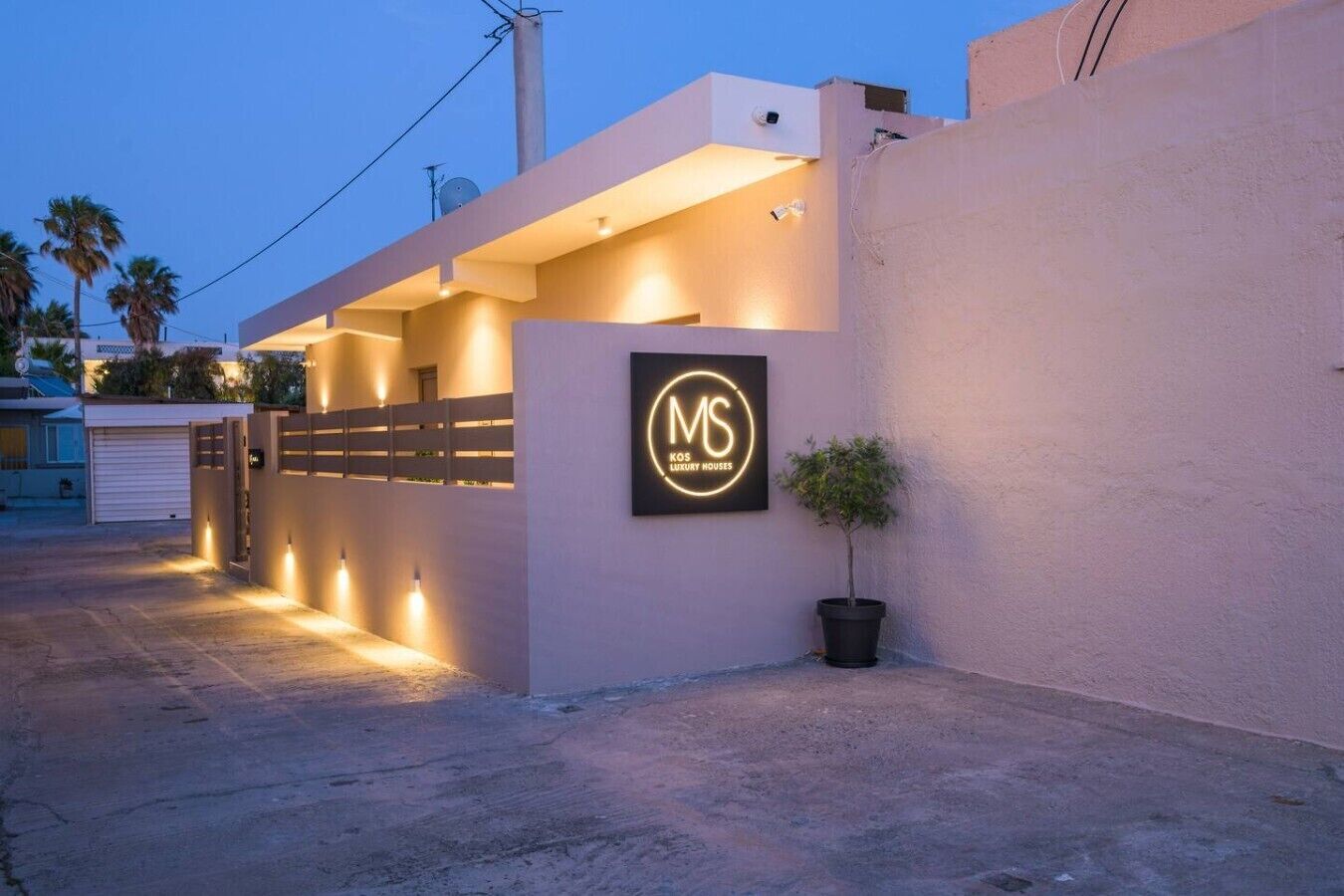 A modern building with a gated entrance, a potted plant, and a sign indicating it's a luxury house.