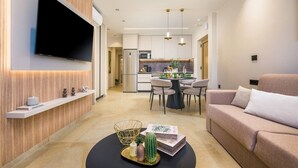Una sala de estar moderna con una televisión de pantalla plana, un sofá, una zona de comedor con sillas y una cocina al fondo.