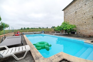 Una piscina con pared de piedra, sillas de descanso y una tortuga hinchable verde.
