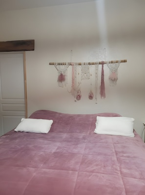 A bed with a pink quilt, two white pillows, and a wall-mounted macrame decoration.