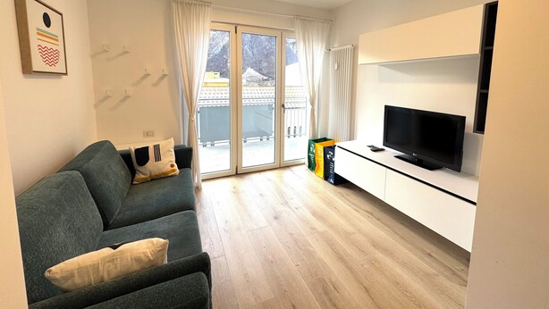 Een moderne woonkamer met een bank, een flatscreen-tv en een schuifdeur die leidt naar een balkon.