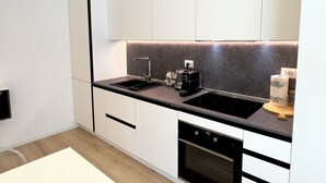 Een moderne keuken met witte kasten, een zwart aanrecht, een inbouwoven en een koffieapparaat.