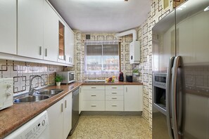 Eine Küche mit weißen Schränken, einem Edelstahl-Kühlschrank, einem Einbauofen und einem Fenster mit Blick auf Gebäude.