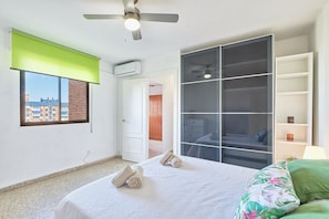 Ein Schlafzimmer mit Bett, einem grünen Fensterrollo, einem Deckenventilator, einem Kleiderschrank und Blick auf Gebäude.