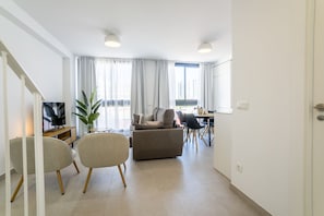 Ein modernes Wohnzimmer mit einer Couch, Sesseln, einem Fernseher und einem Essbereich.