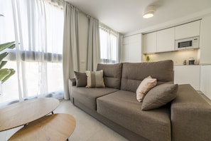 Ein modernes Wohnzimmer mit einer Couch, einem Couchtisch und einer Küchenzeile mit einer Mikrowelle.