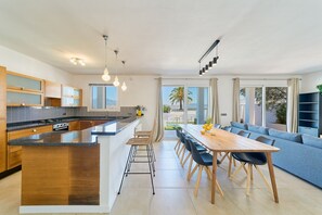 Eine moderne Küche mit Kochinsel, Essbereich mit langem Tisch und Stühlen sowie Wohnbereich mit Sofa und Fernseher.