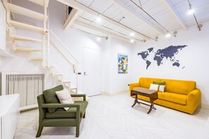 Ein modernes Wohnzimmer mit einem grünen Sofa, einem gelben Sofa und einem kleinen Tisch. An der Wand hängt eine Weltkarte und eine Treppe mit weißen Geländern.