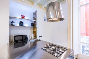 A modern kitchen with a stainless steel countertop, a built-in microwave, a gas stove, and a hanging pendant light. - Chiaia Prestige by Napoliapartments (Naples)
