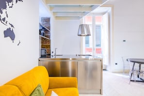 Eine moderne Küche mit einer Edelstahl-Kochinsel, einem leuchtend gelben Sofa und freiem Blick nach draußen.