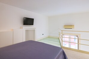 A bedroom with a bed, a television, an air conditioning unit, and a window with a view of buildings. - Chiaia Prestige by Napoliapartments (Naples)