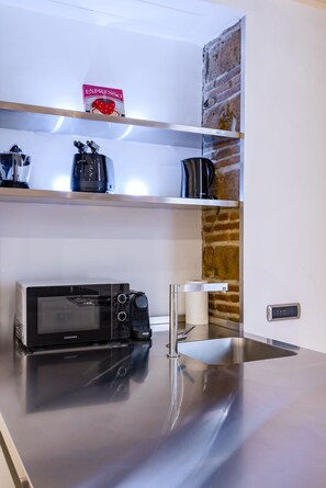 A kitchen with a microwave, a coffee maker, and a shelf with a coffee box. - Chiaia Prestige by Napoliapartments (Naples)