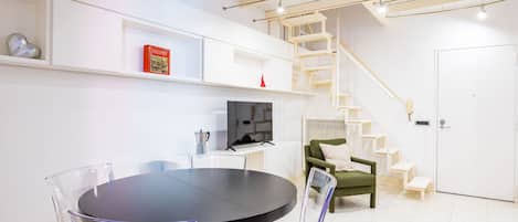 A modern living room with a round table, chairs, a television, and a staircase.