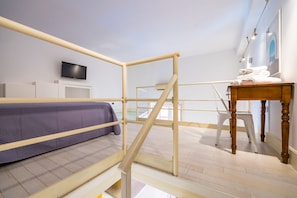 Ein Schlafzimmer mit Bett, Fernseher, Holztisch und Fenster.
