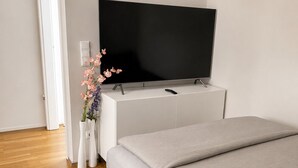 A bedroom with a bed, a TV on a white cabinet, and a door leading to another room.