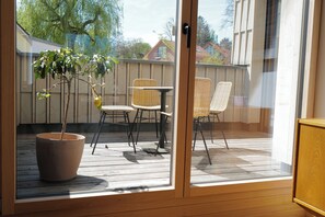 Una terraza de madera con una planta en maceta, sillas de mimbre y una mesa.