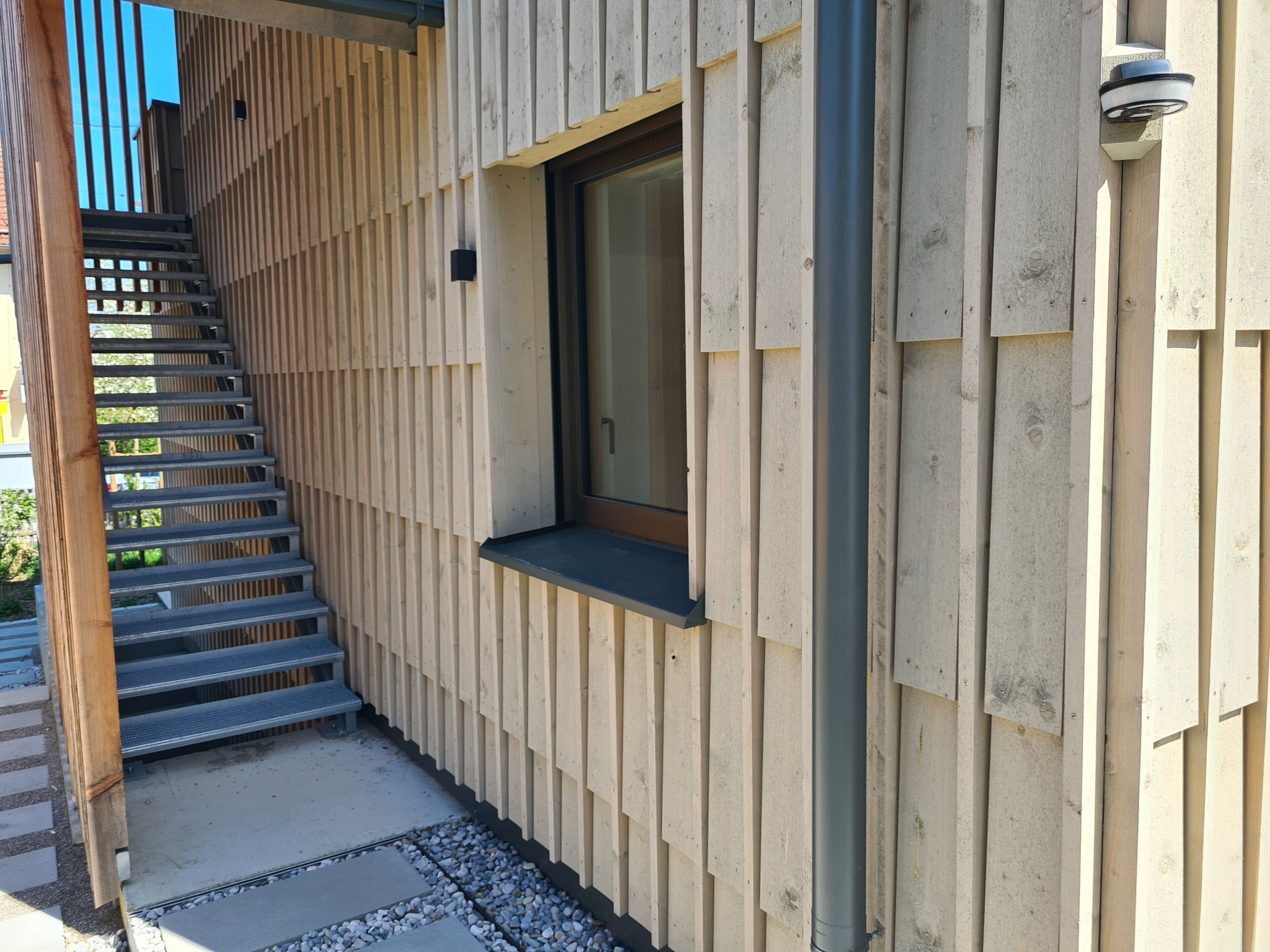 Eine Holzfassade mit einer Metalltreppe, die zu einer Tür führt.
