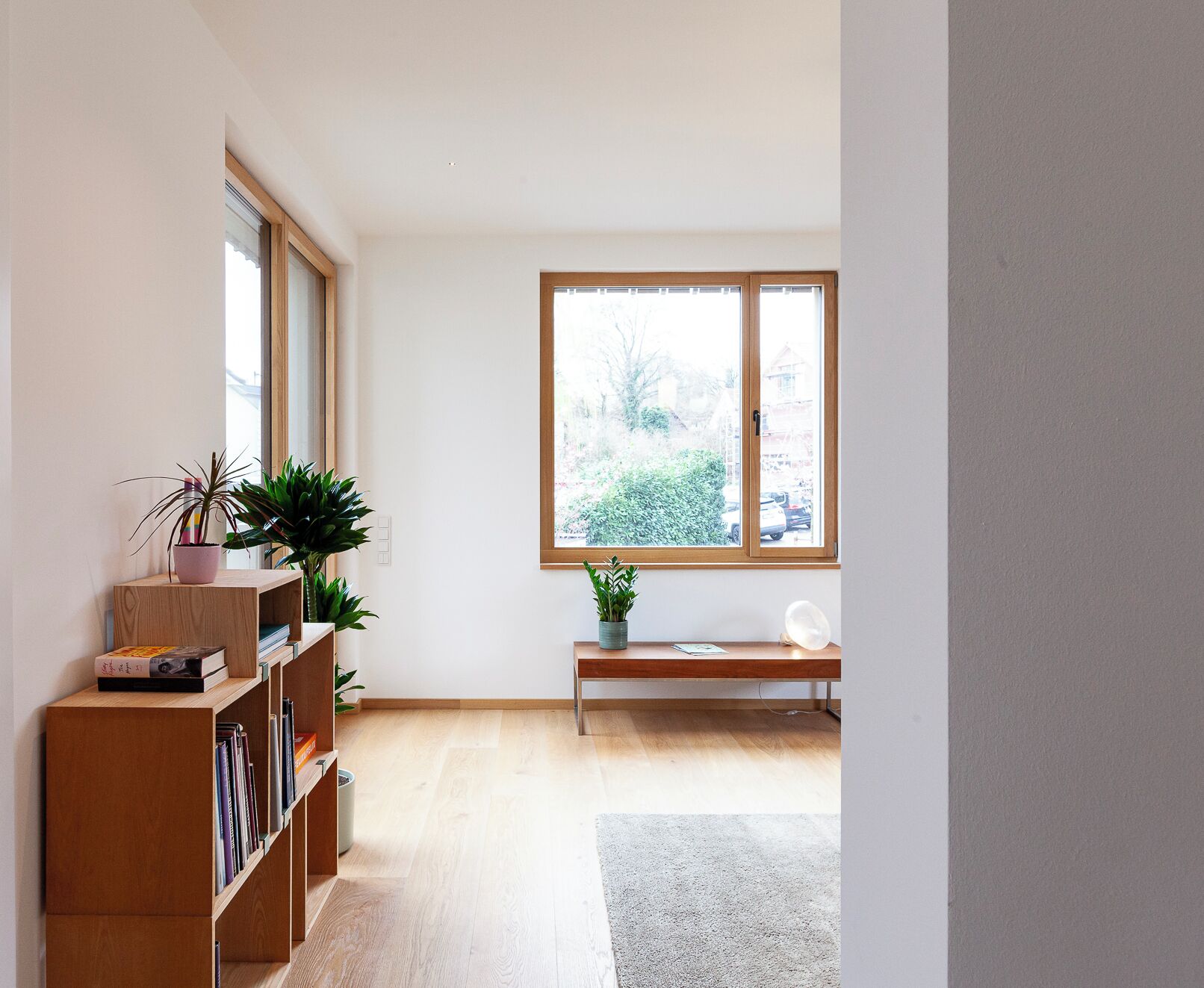 Ein Zimmer mit Holzregal, einer Bank und einem großen Fenster mit Blick auf Grünflächen.