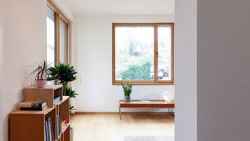 Ein Zimmer mit Holzregal, einer Bank und einem großen Fenster mit Blick auf Grünflächen.