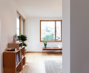 Una habitació amb una biblioteca de fusta, una banca i un gran finestral amb vista a vegetació.