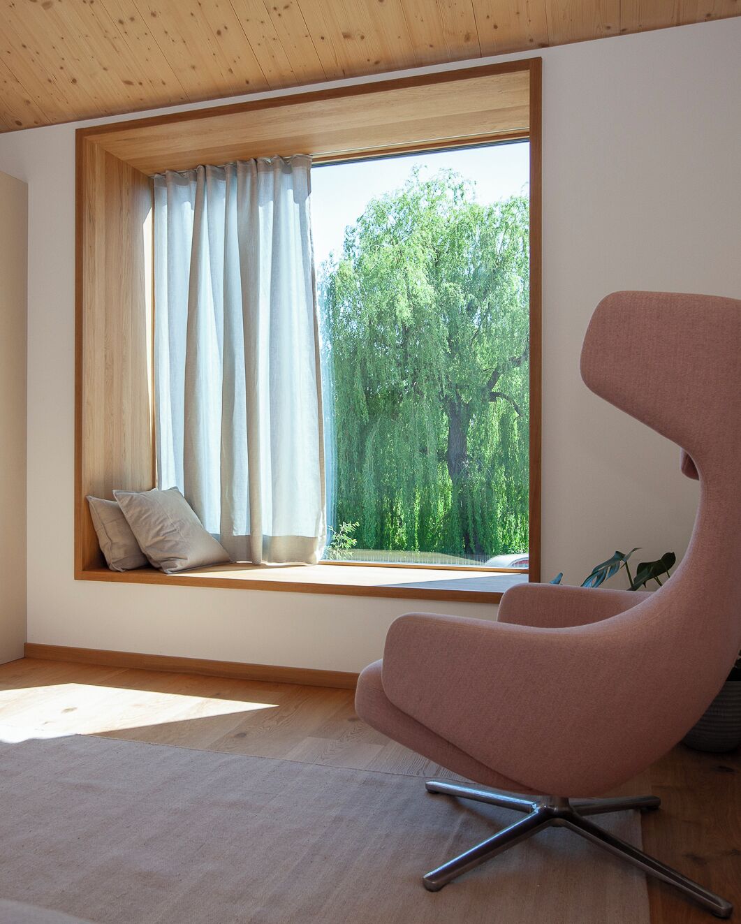 Ein Zimmer mit großem Fenster, einem modernen Sessel und Holzboden.