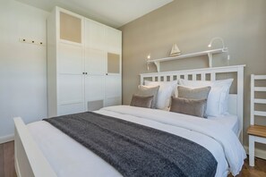 A bedroom with a bed, white wardrobe, and a shelf with a lamp. - Cozy vacation rental with a balcony near the beach and forest (Ostseebad Koserow)