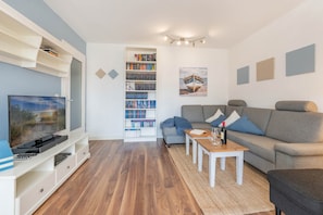 Un salon avec un téléviseur, une bibliothèque, un canapé gris et une petite table basse.