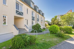 A multi-story residential building with a front entrance, steps, and a small garden area with bushes and a pathway. - Cozy vacation rental with a balcony near the beach and forest (Ostseebad Koserow)