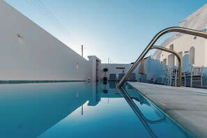 Ein klares, blaues Schwimmbecken mit einer Metallleiter, weißen Wänden und einigen Liegestühlen.