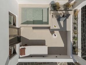 A modern outdoor living area with a seating arrangement, a small table, and a planter with plants. - Sifneos House (Paros)