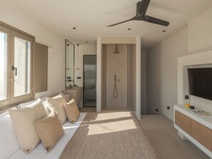 A modern bedroom with a large bed, a walk-in closet, a built-in TV, and a shower. - Sifneos House (Paros)