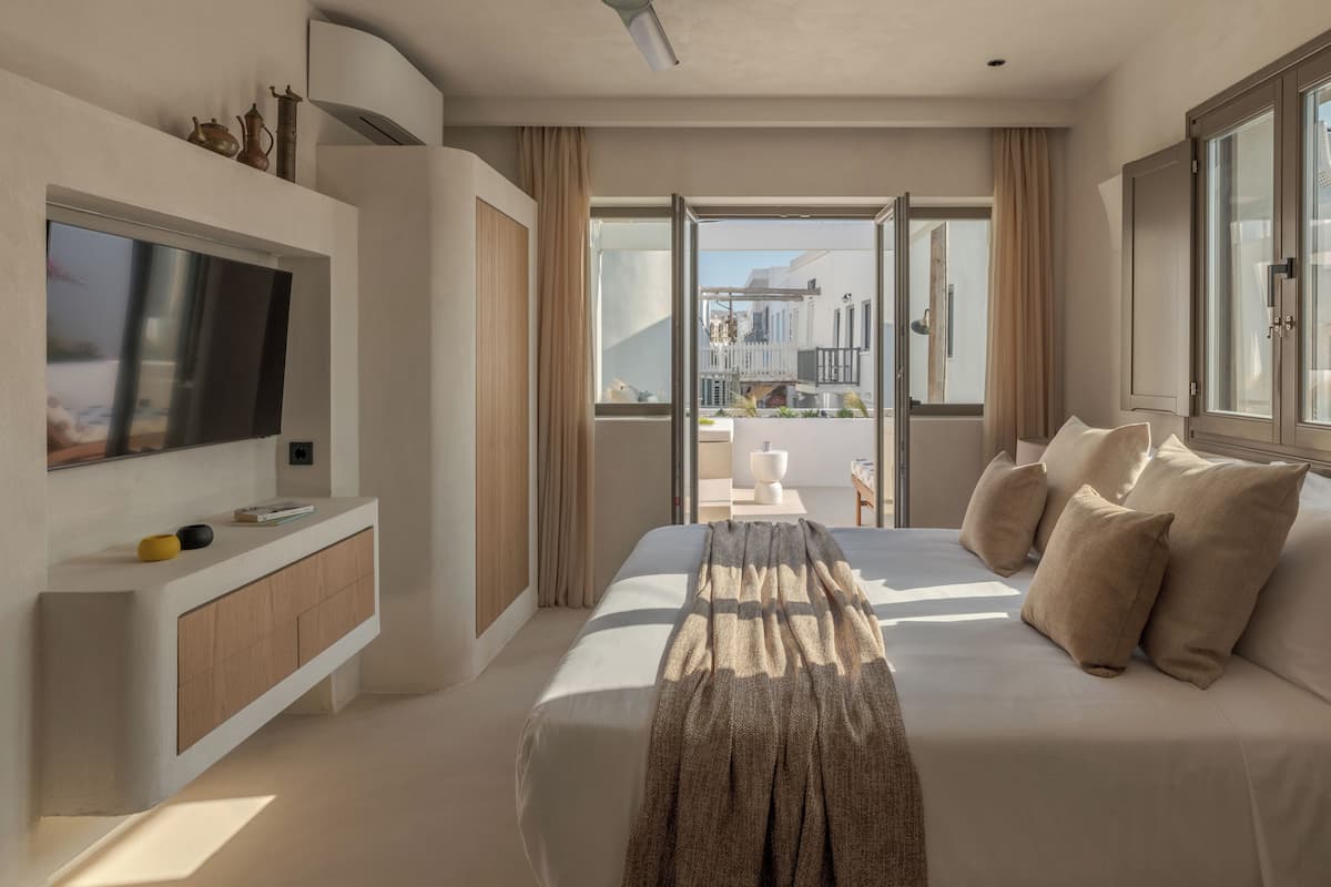 Une chambre d’hôtel moderne dotée d’un grand lit, d’une télévision à écran plat, d’un ventilateur de plafond et d’un balcon offrant une vue sur la ville.
