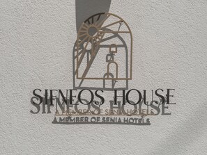 A logo with a sun and a bicycle, and the text 'SINEOS HOUSE A MEMBER OF SENIA HOTELS.' - Sifneos House (Paros)