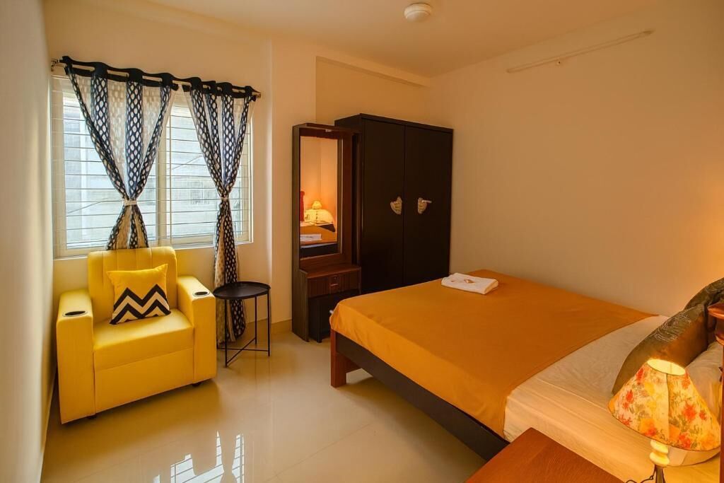 A hotel room with a bed, a chair, a wardrobe, a desk, and a lamp.