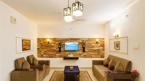 A modern living room with a flat-screen TV, two sofas, a coffee table, and decorative wall shelves.
