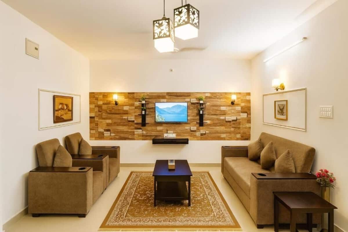A modern living room with a flat-screen TV, two sofas, a coffee table, and decorative wall shelves.