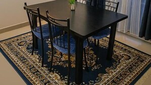 A dining area with a table, chairs, a rug, a painting, and curtains.