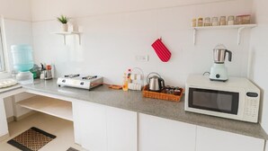 A kitchen with white cabinets, a microwave, a gas stove, a kettle, and a blender.