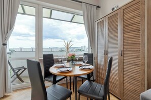 Uma sala de jantar com uma mesa posta para quatro pessoas, quatro cadeiras, um vaso com flores e vista para a cidade através de grandes janelas.