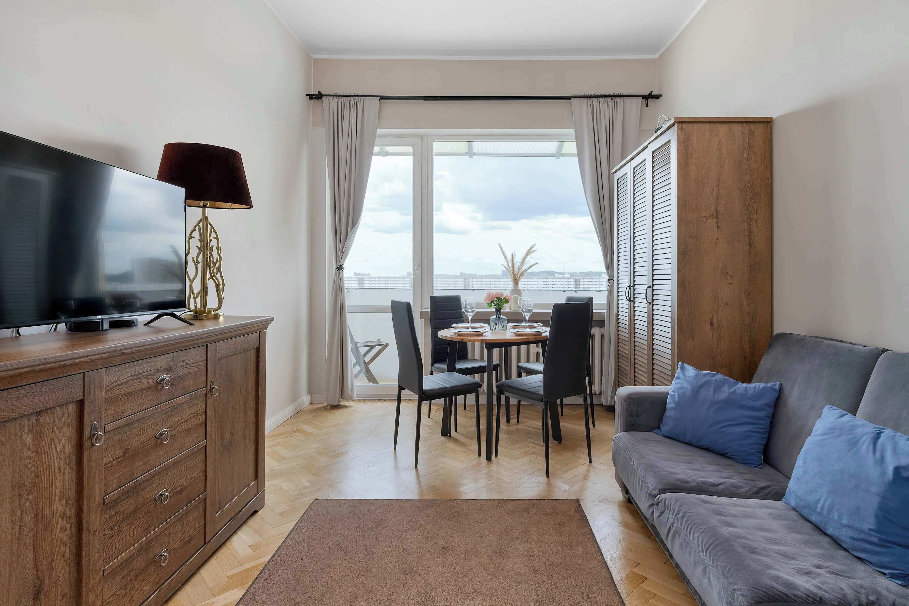 Un salon comprenant un canapé, un téléviseur, un meuble en bois et un coin repas avec des chaises et une table.