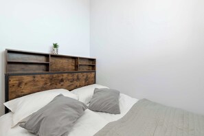 Uma cama com cabeceira de madeira, duas almofadas, um edredom acolchoado e um pequeno vaso com planta na cabeceira.