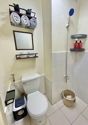 Casa de banho com sanita, chuveiro, lavatório e prateleira com toalhas.
