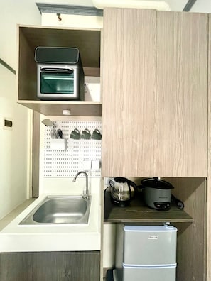 Uma cozinha compacta com pia, cafeteira, torradeira e geladeira pequena.