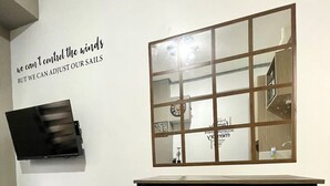 A compact room with a bed, a desk with two chairs, a small table with a plant, and a wall-mounted shelf. - Urban Deca Tower Mandaluyong-Cozy Stay (Mandaluyong City)