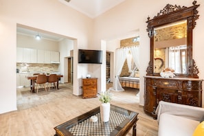 A spacious living area with a dining table, chairs, a coffee table, a TV, a mirror, and a kitchen in the background. - Absinthia Legacy Country House with Shared Garden, Wi-Fi and Air Conditioning (Soroni)