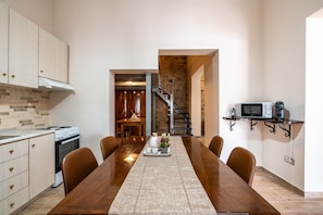 A modern kitchen with wooden cabinets, a dining table with chairs, a microwave, and a staircase leading to another room. - Absinthia Legacy Country House with Shared Garden, Wi-Fi and Air Conditioning (Soroni)