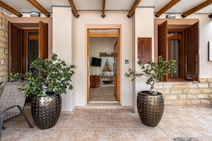 A hallway with two large potted plants, wooden shutters, and a television in the background. - Absinthia Legacy Country House with Shared Garden, Wi-Fi and Air Conditioning (Soroni)